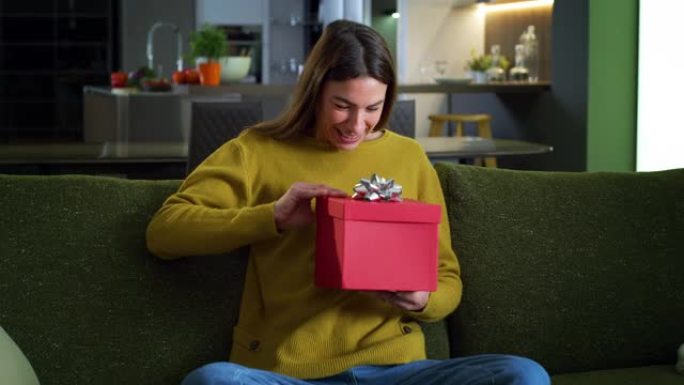 年轻幸福的女人打开红色礼品盒的肖像，对她生日时收到的礼物感到兴奋和惊讶。女性早上在家打开圣诞礼物