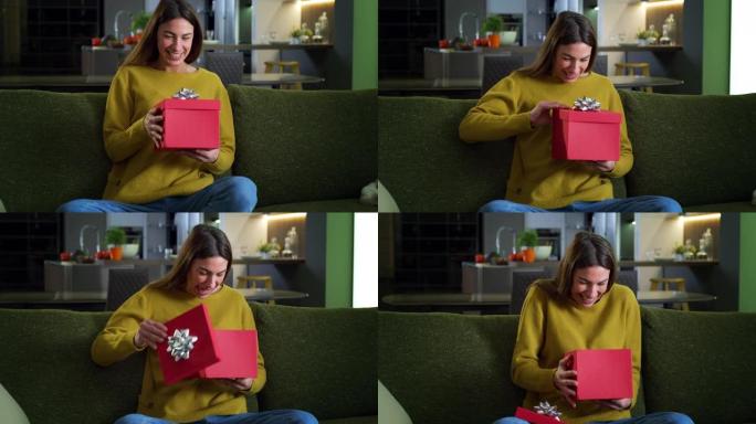 年轻幸福的女人打开红色礼品盒的肖像，对她生日时收到的礼物感到兴奋和惊讶。女性早上在家打开圣诞礼物