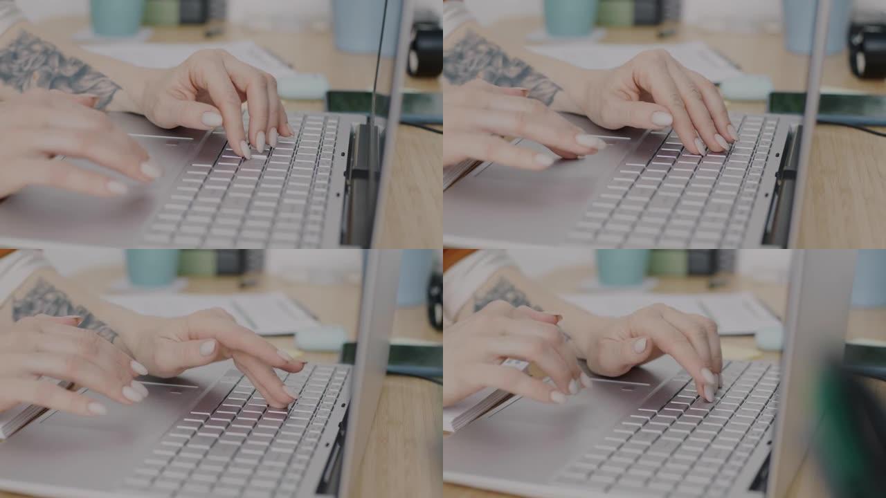 使用笔记本电脑在办公桌上打字的女性纹身手的特写镜头