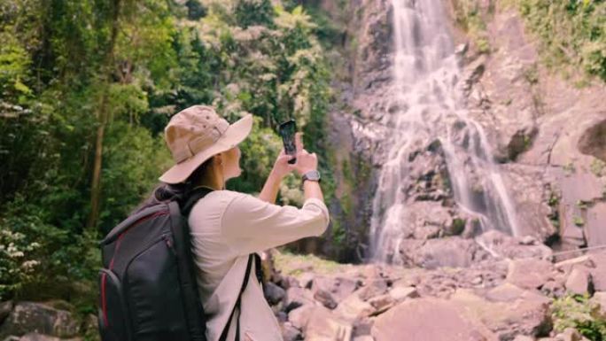 亚洲女孩徒步旅行用手机拍照瀑布。