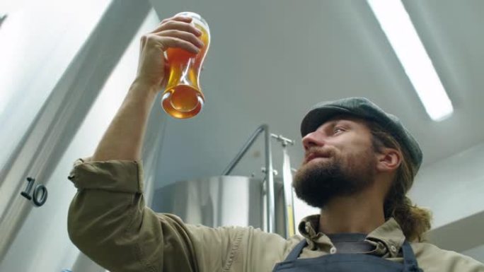 微笑的啤酒厂技术员正在检查一杯新鲜的啤酒