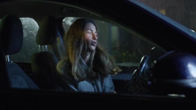 透过窗户看: 一个年轻女子在雨夜坐在车里，在收音机里听一首歌的肖像。女司机一起跳舞唱歌。她在车里等着