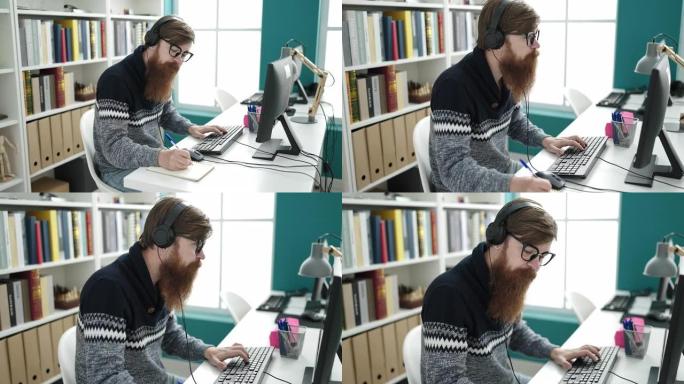 年轻的红发男子学生在图书馆大学使用电脑和耳机在笔记本上写字