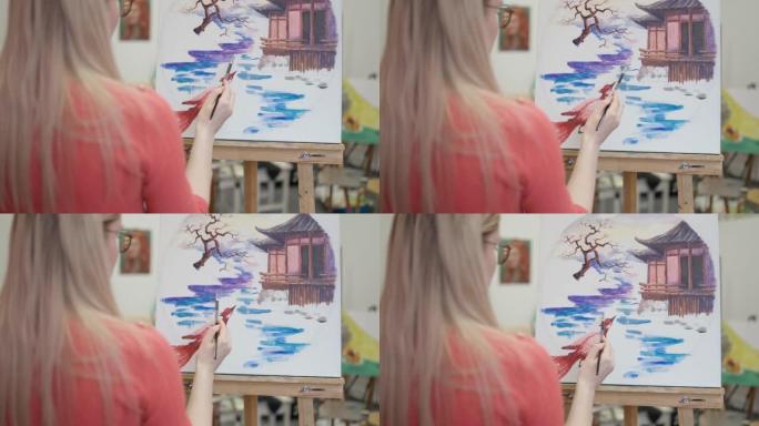 在工作室里，年轻的金发女子用丙烯酸颜料在画布上绘画