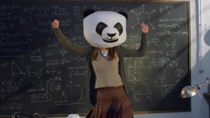 有趣的镜头: 戴着熊猫面具的女老师用数学公式在黑板前跳舞。大学或大学教室的科学研究员为她的日常工作增