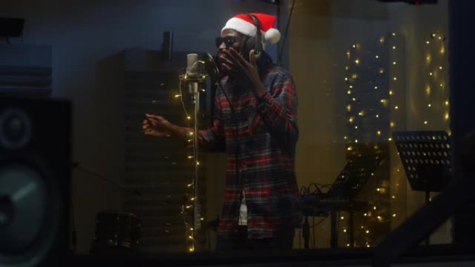 一位职业男性黑人歌手的肖像在录音室为他的圣诞节专辑录制了一首歌。戴着圣诞老人帽子的非洲年轻艺术家喜欢