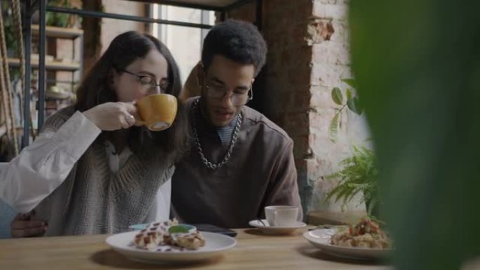女孩和男孩幸福的夫妇看着智能手机屏幕在咖啡馆里聊天和喝咖啡