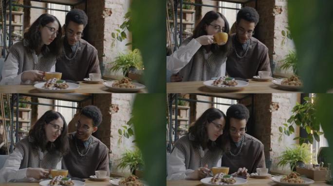 女孩和男孩幸福的夫妇看着智能手机屏幕在咖啡馆里聊天和喝咖啡
