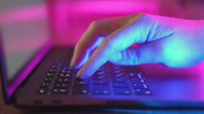 晚上在笔记本电脑上打字的人。女性使用键盘，用手指摇动按钮。互联网安全，网络攻击。时尚霓虹灯。紫外线红
