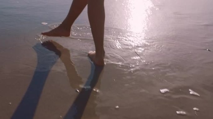 近距离女子脚赤脚走在海滩上日落留下脚印的沙滩女游客在暑假