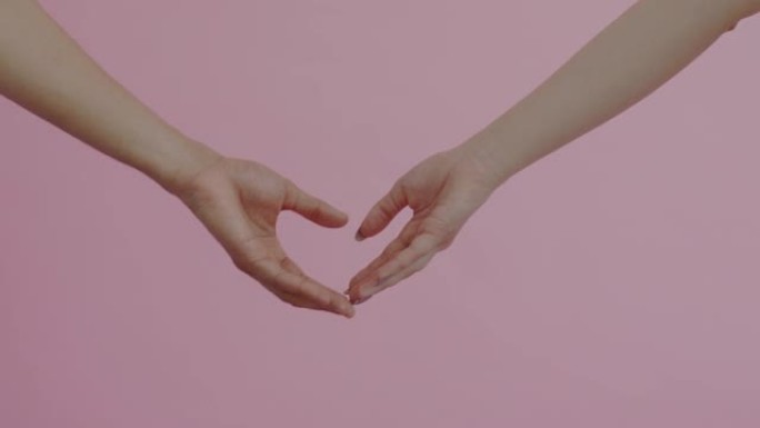 爱心人士的手臂相互接触，在粉红色背景上抚摸心形