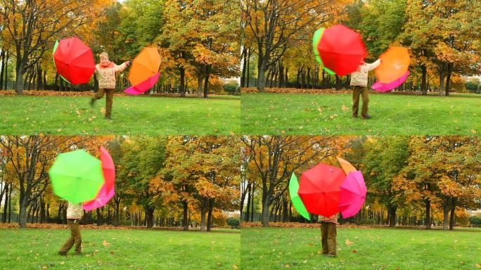 男孩在秋季公园用雨伞旋转