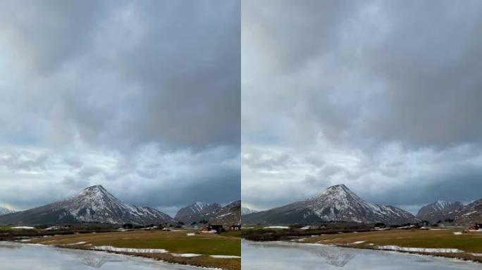 在寒冷的晴天，天空和云密布，美丽的白色冬季仙境全景，雪山山顶映衬在水晶般清澈的冰湖中。挪威峡湾山。
