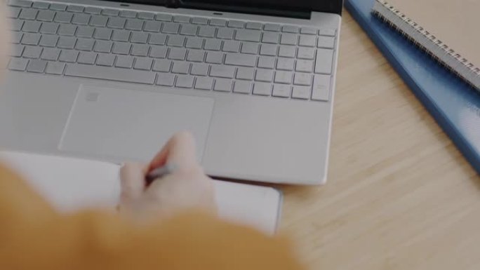 使用笔记本电脑在办公桌上打字和书写信息的女性手的特写