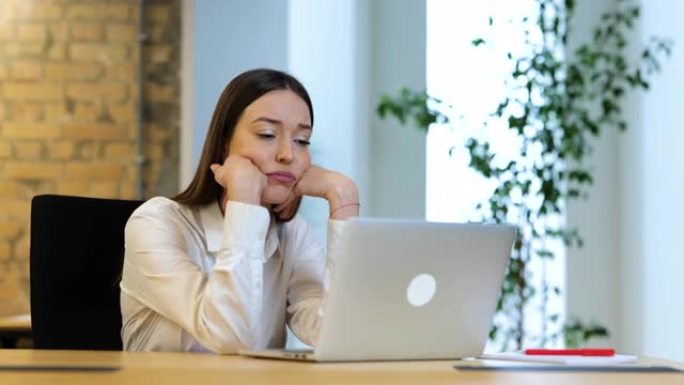 穿着白色衬衫的深色长发的白人女性正坐在电脑前，工作着，看上去很沮丧。慢动作视频。