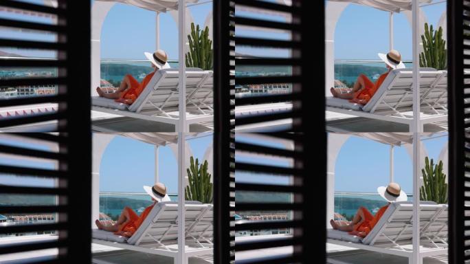 女人在日光浴床放松，在豪华屋顶顶楼露台享受暑假，可以看到海景。后视图