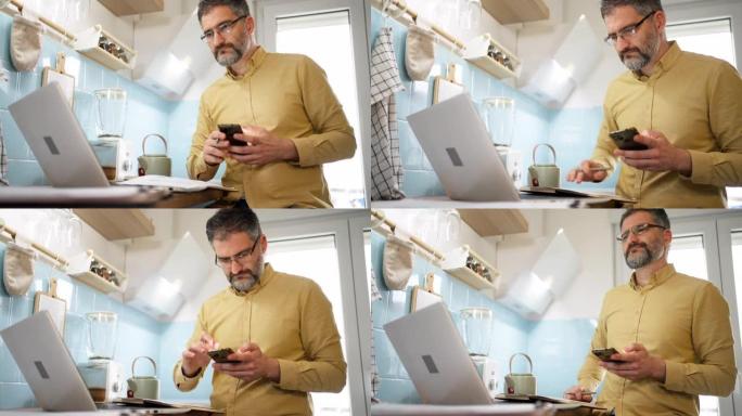 男人在现代厨房的笔记本电脑上工作时使用手机
