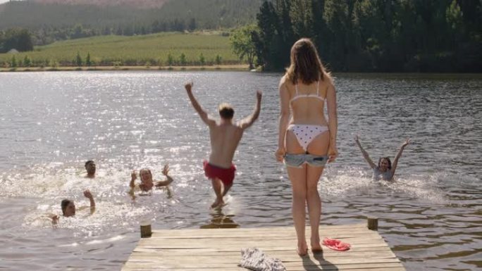 男人和女人脱衣服从湖边的码头上跳下来，在假期里一起享受夏天的下午