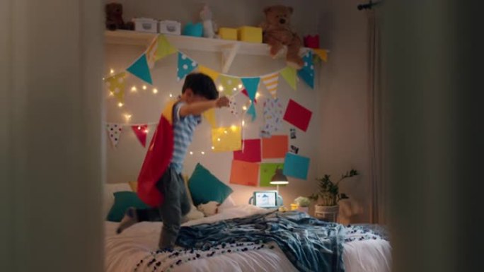 快乐的小男孩穿着戏服跳上床在家里五颜六色的卧室里玩游戏享受嬉戏的想象力