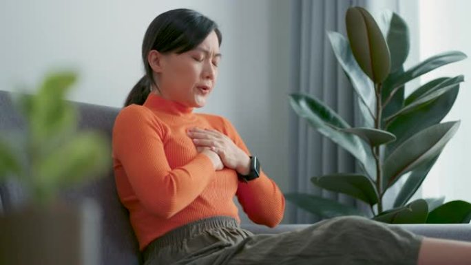 亚洲妇女因坐在家里客厅的沙发上而感到胸痛。