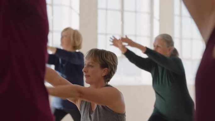 瑜伽课的健康成熟女性练习战士姿势享受早晨体育锻炼工作室