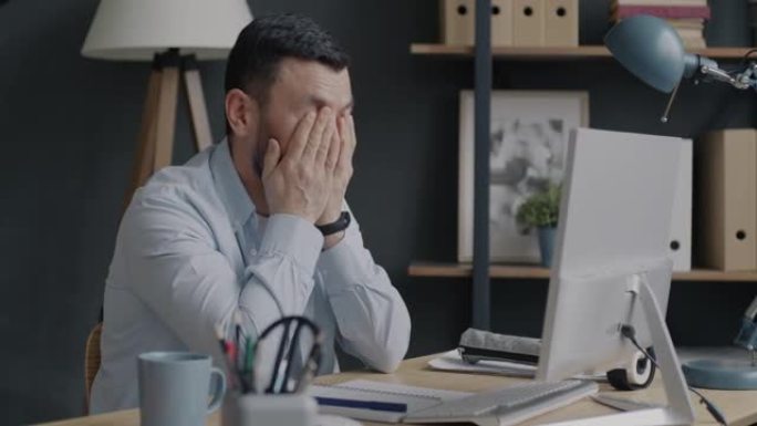 疲惫的商人肖像看着电脑屏幕叹息，在办公室感到筋疲力尽