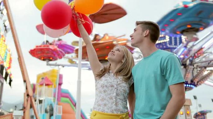 在游乐场上拿着气球的年轻夫妇