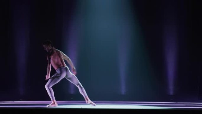 年轻优雅的古典芭蕾舞男舞者在剧院舞台上表演，并带有戏剧性的聚光灯照明。运动男子跳舞并排练舞蹈表演