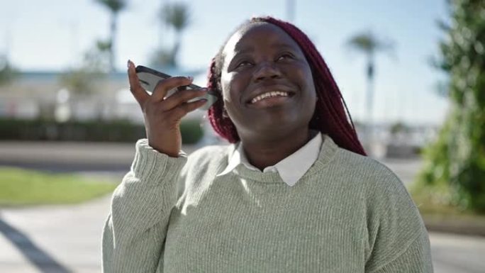 编织头发的非洲妇女在街上用智能手机收听语音信息