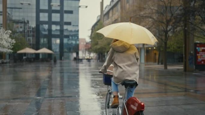 SLO MO年轻女子带黄伞在城市雨中骑自行车
