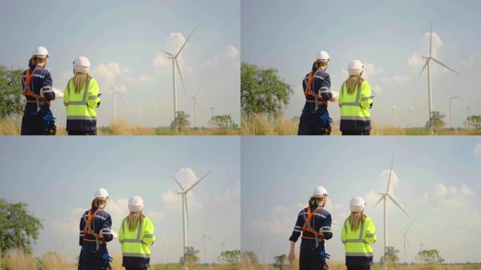 两名工程师的后视图高加索男人和女人戴着安全帽和护目镜谈论蓝图行走，以验证风力涡轮机是否正确有效地运行