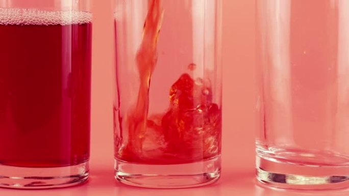 石榴汁被倒入粉红色背景的玻璃酒杯中。慢动作。