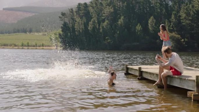 年轻男子抓住女人和她一起在湖中跳跃，在水中泼水一群朋友在夏天的下午闲逛，享受假期