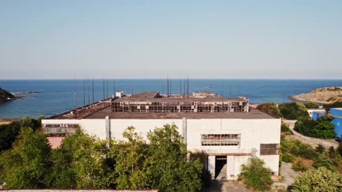 废弃的海滨工业仓储综合体工厂阳光明媚的一天海岸蓝色水FPV直飞通过屋顶杆