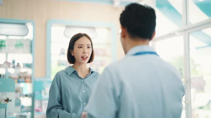 亚洲成熟男性药剂师在药房过道向年轻女性顾客解释。药剂师在药房向年轻女性顾客解释。
