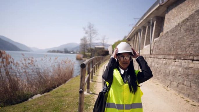 在城市环境中，穿着背心，防护眼镜和安全帽头盔的女工程师侦察施工现场。