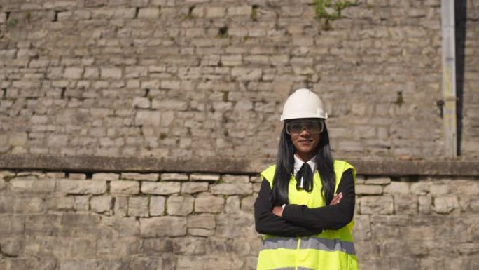 女工程师站在背心，防护眼镜和安全帽头盔上，对着镜头微笑