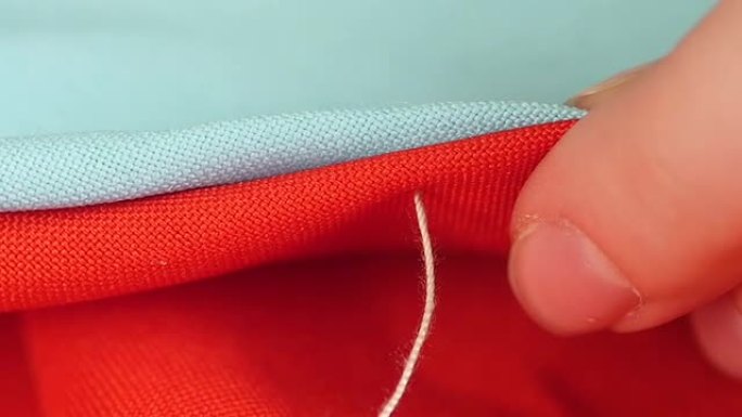 女人的手在红色和蓝色的衣服上用针，白线和顶针缝制，特写，慢动作