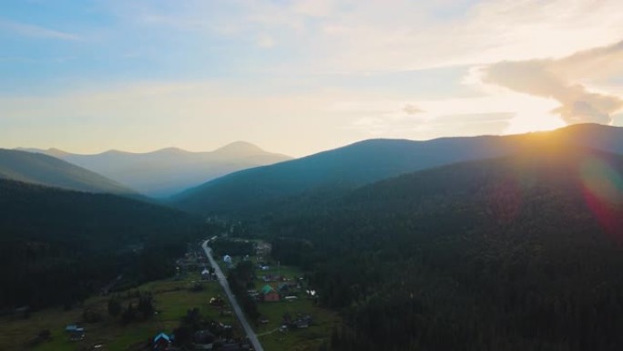 在明亮的日落时分，在高山峰和深色松树林之间的小山村房屋上，雾蒙蒙的夜晚的鸟瞰图。黄昏时野生山地林地的