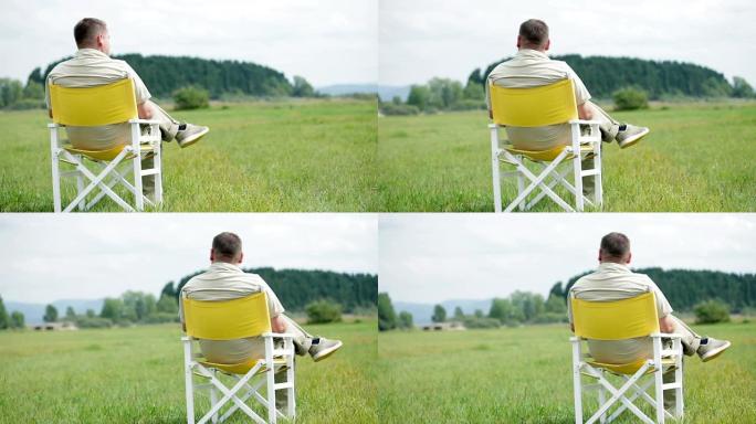 高清: 男人坐在白色野餐椅上观察自然