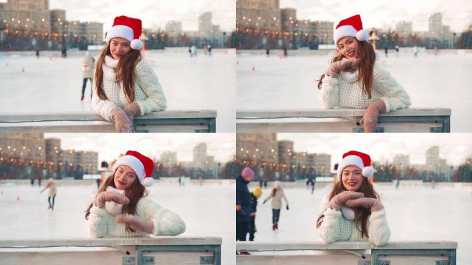 年轻微笑的女人圣诞老人帽子在外面的溜冰场上滑冰，穿着白色毛衣。圣诞假期，活跃冬季休闲手持效果。业余高
