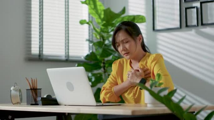 坐在家庭办公室的笔记本电脑上患有胸痛的亚洲女性。