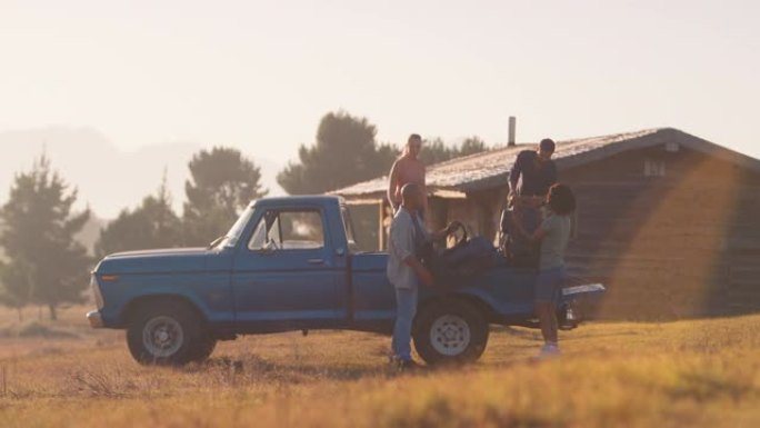 一群朋友在日落时分到乡村小屋的公路旅行中从卡车上卸下背包-慢动作拍摄