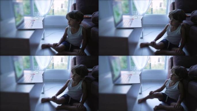 小男孩坐在家里的地板上看笔记本电脑上的动画片。盯着娱乐媒体的孩子