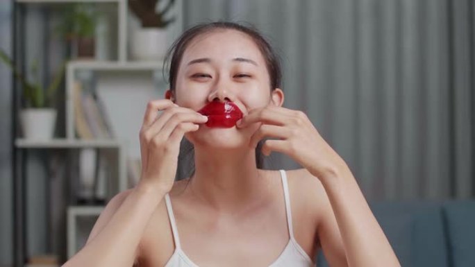 美丽的年轻亚洲女性使用胶原蛋白唇膜干裂的嘴唇，然后在家里照顾皮肤时对着镜头微笑