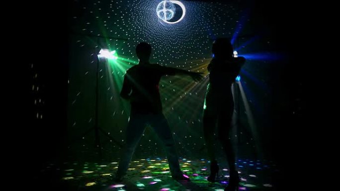 女孩和男孩在夜总会现场跳舞。掷铁饼器美丽地照亮了房间