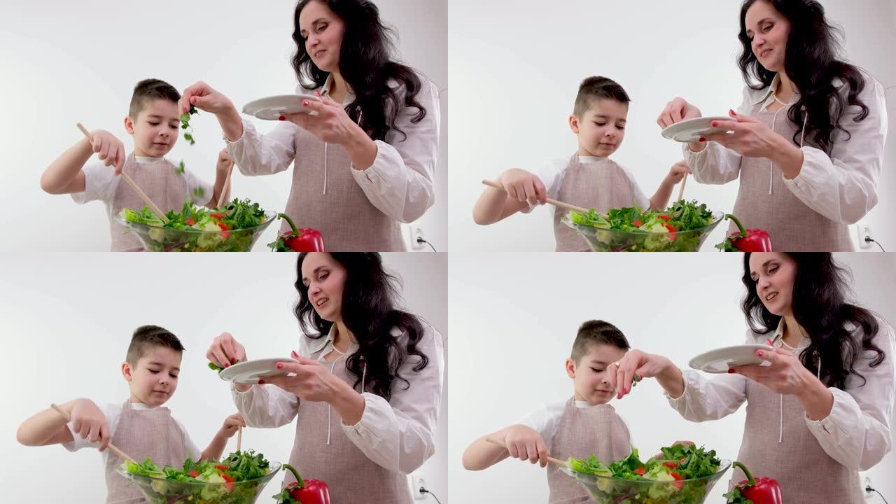 漂亮的家庭主妇看着小儿子在家里的现代厨房里撕扯新鲜的生菜叶在餐桌上煮沙拉