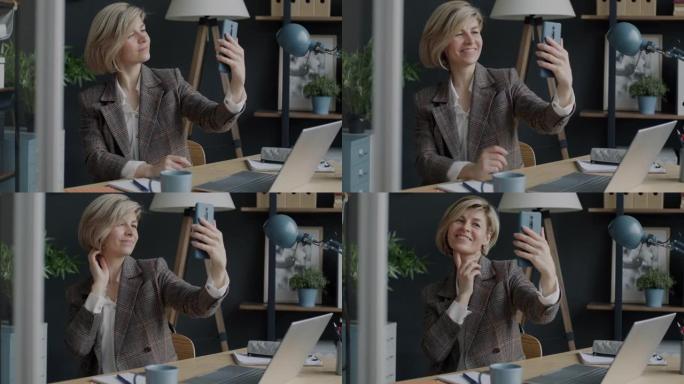 快乐的女商人在办公室里用智能手机摆姿势自拍并在室内微笑的肖像