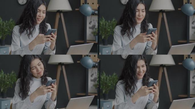 快乐的年轻亚洲女士用智能手机微笑着在办公室享受交流