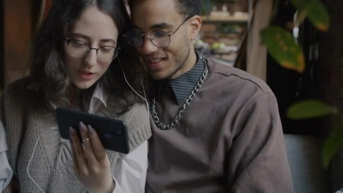 快乐的混血儿夫妇一起坐在咖啡馆里看着智能手机屏幕聊天